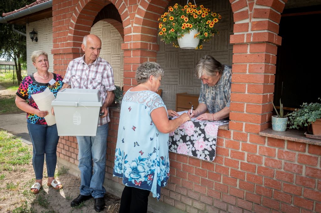 Egy idős nő (j) választási névjegyzékben szereplő adatait egyeztetik, mielőtt leadja a szavazatát a házában a mozgóurnás szavazáson az önkormányzati, európai parlamenti (EP-) és nemzetiségi választásokon Petőfiszálláson 2024. június 9-én. MTI/Ujvári Sándor