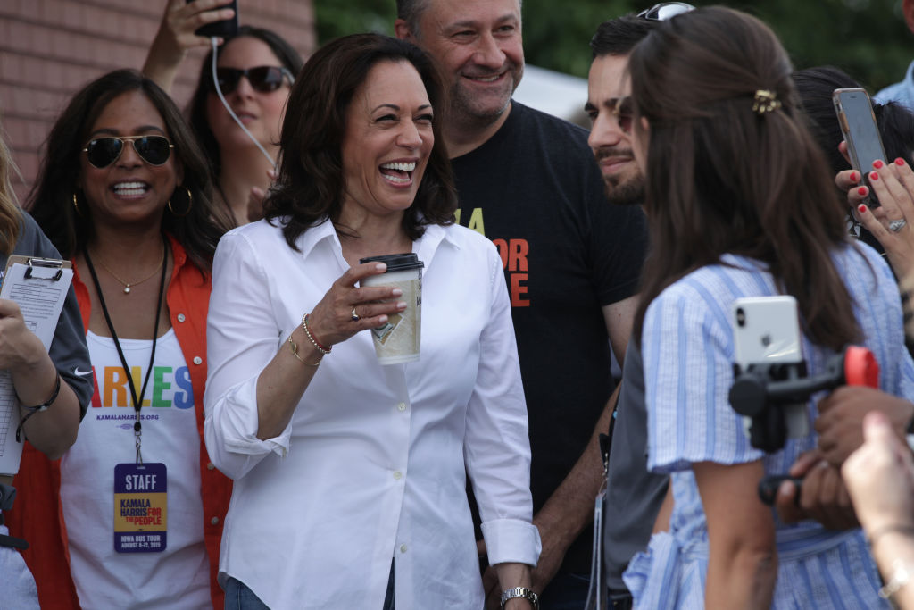 Kamala Harris kávéval a kezében nevet fehér zakóban