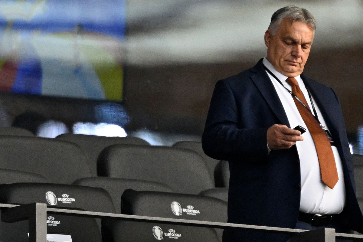 Orbán Viktor a mobiltelefonját nyomogatja egy stadionban.