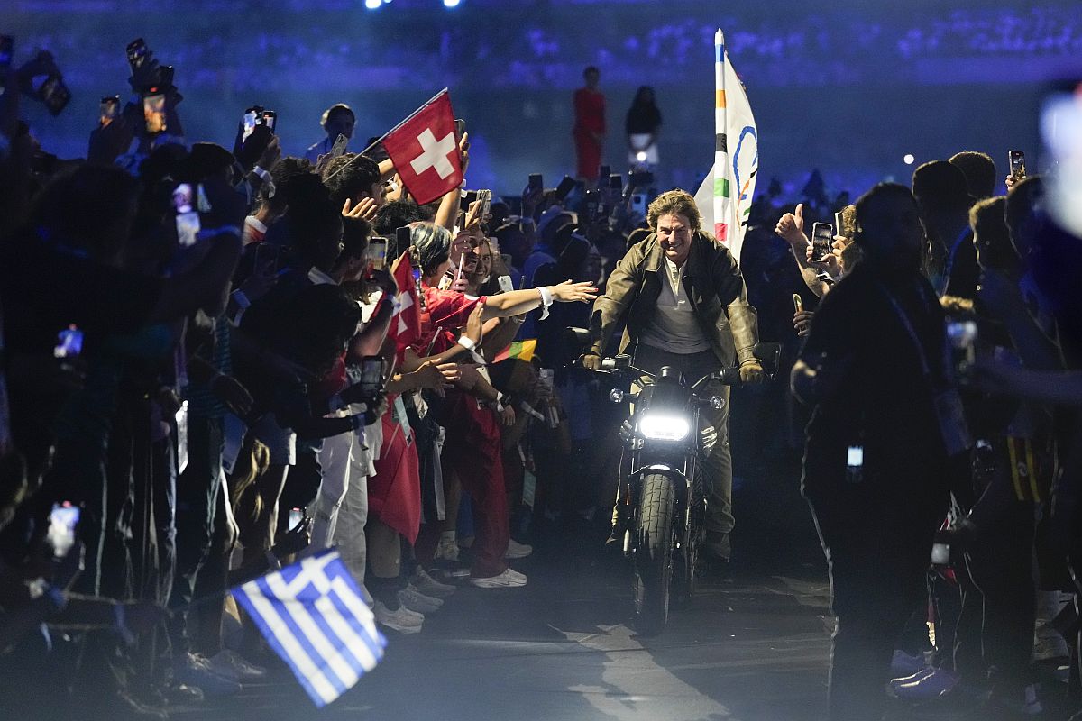 Tom Cruise motoron ül, mögötte az olimpiai zászló.