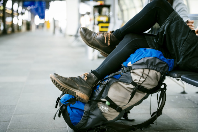 Turista ül egy váróteremben, barna bakancsban kék barna túrazsák mellett