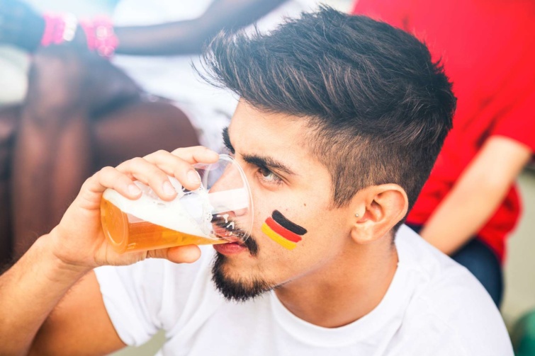 Fiatalember német színekkel az arcán műanyag pohárból sört fogyaszt