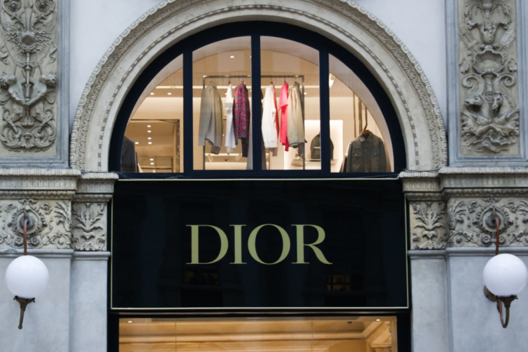 Dior üzlet ablakon keresztrül színes ruhák látszanak a fogason, előtérben a cégér.