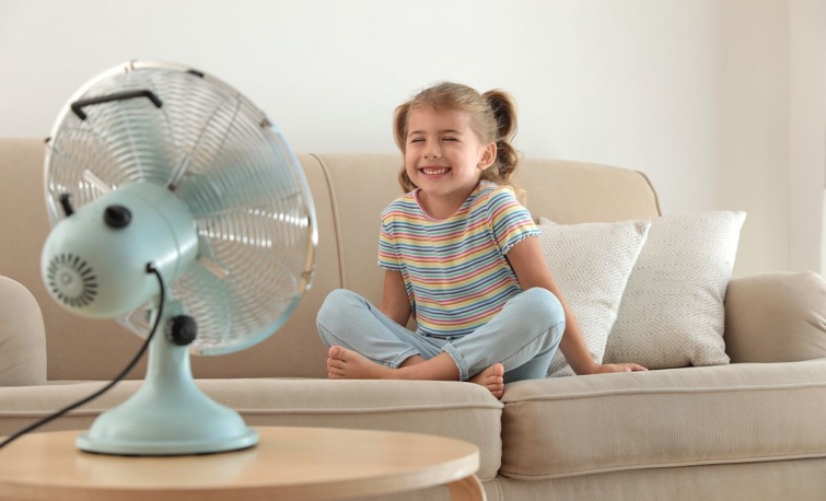 Egy kanapén ülő gyerek a ventilátor széláramában.