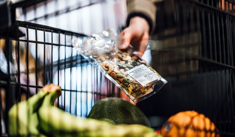 Egy vásárló egy zacskó diófélét tart a kezében a bevásárlókocsi fölött a boltban.